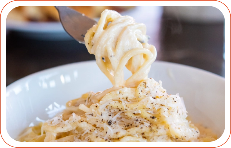 Close-up of a fork twirling spaghetti onto it. The spaghetti is covered in white sauce.