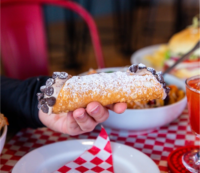 A hand holds a cannoli with chocolate chips on each end.
